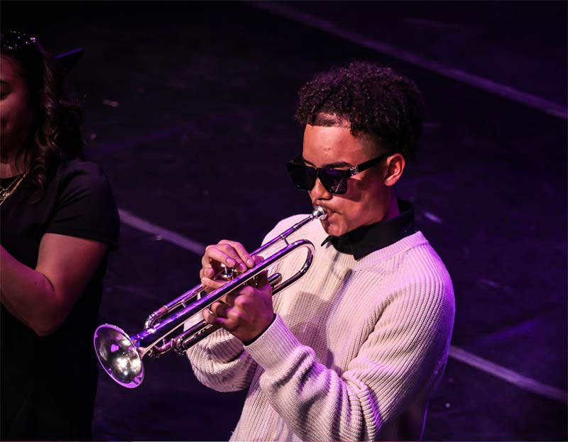 A student in sunglasses playing trumpet on stage
