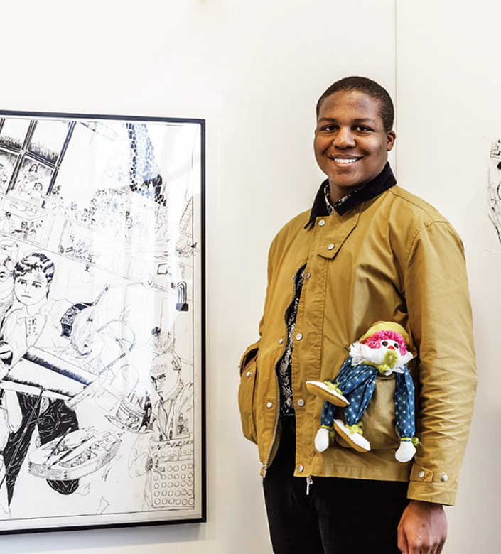 Cam Collins standing in a gallery alongside framed drawing